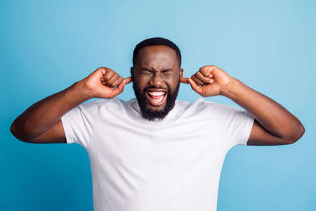 Photo of woried annoyed man fingers cover ears wear white t-shirt over blue backgroundの写真素材