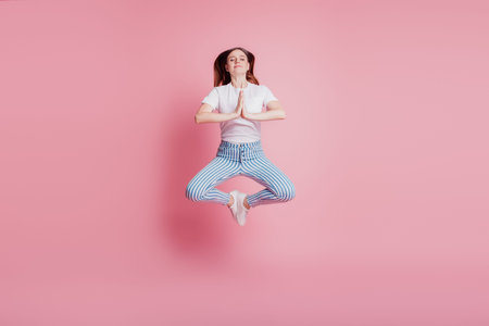 Portrait of playful crazy girl jumping in the air meditate lotus pose on pink background