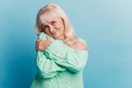 Photo of old lady embracing herself isolated on blue backgroundの写真素材