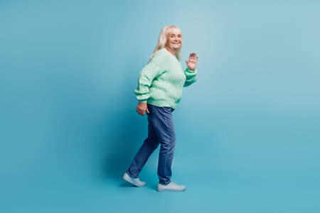 Candid old woman walk wave hand isolated over blue background