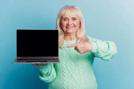 Retired granny hold laptop show point finger display isolated on blue backgroundの写真素材