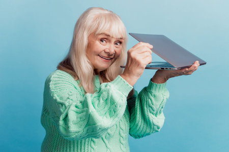 Attractive grey-haired old woman hold laptop isolated on blue background