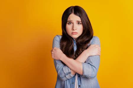 Portrait of a freezing pretty woman embrace shoulders sad face on yellow backgroundの写真素材