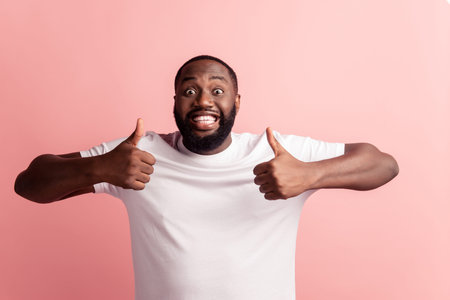 Portrait of happy afroamerican handsome bearded man showing thumb up gesture on pink wall