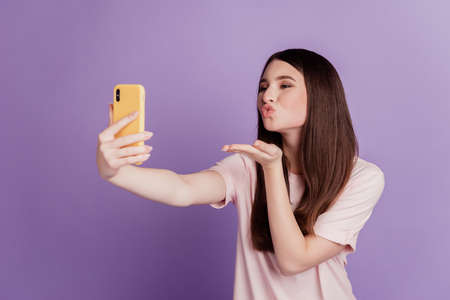 Photo of cheerful cute young woman hold smartphone take selfie hold palm blow air kissの写真素材