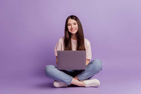 Photo of girl with laptop sit floor look camera on purple backgroundの写真素材