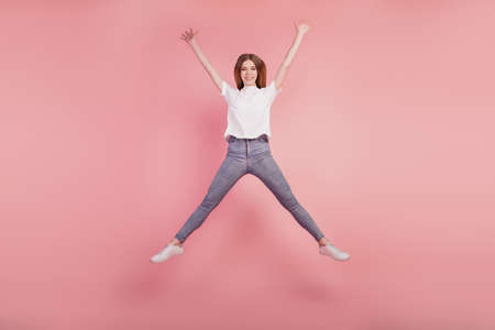 Photo of energetic pretty girl jump high up on pink backgroundの写真素材