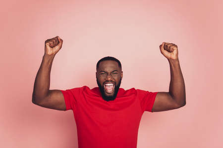 Dark skin guy raise fists victory look empty space isolated over pink backgroundの写真素材