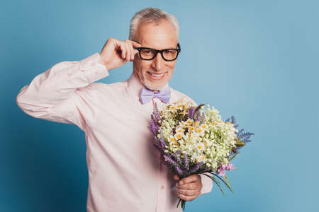 Portrait of husband aged guy with wild flowers bunch prepare for date ob blue backgroundの写真素材
