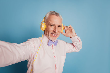 Portrait of enthusiastic mature macho taking selfie for social web page listening headphonesの写真素材