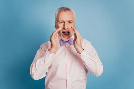 Elderly gray-haired man in shirt bow tie screaming information near mouthの写真素材