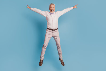 Full length view of handsome man jumping up having fun isolated blue background