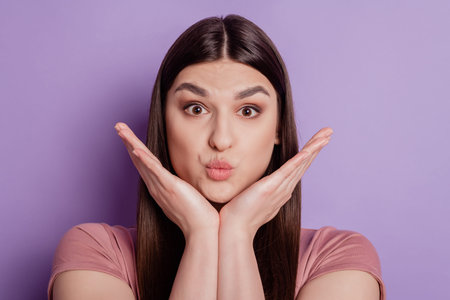Portrait of pretty girl blowing air kiss with pout lips hands touchc chin isolated on purple color...