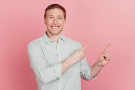 Portrait of nice attractive guy indicate forefinger empty space shiny smile on pink backgroundの写真素材