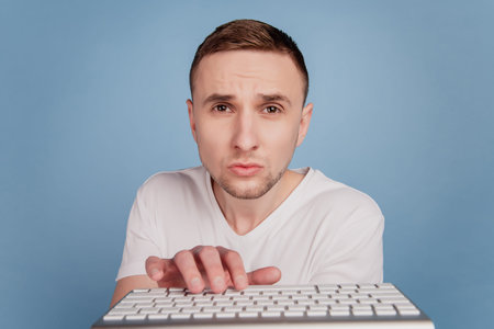 Businessman in white t-shirt typing on computer keyboard email work focused isolated over blue color...