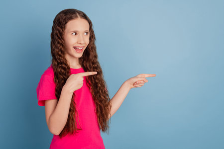Portrait of curious promoter small lady indicate fingers empty space look side on blue background