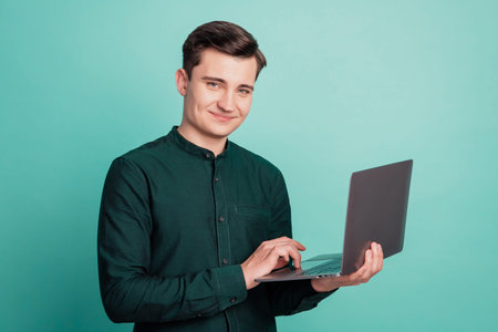 Portrait of positive freelancer man hold netbook chatting look camera on teal background