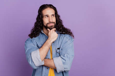 Portrait of attractive minded happy young man finger chin look empty space on purple wallの写真素材