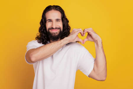 Portrait of affectionate charming guy fingers show heart symbol on yellow backgroundの写真素材