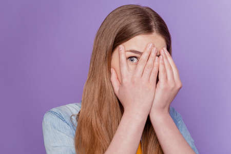 Portrait of frightened lady palm cover face peek eye wear jeans clothes on purple backgroundの写真素材