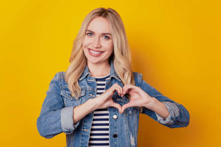 Portrait of romantic dreamy girlfriend lady show heart gesture on yellow backgroundの写真素材
