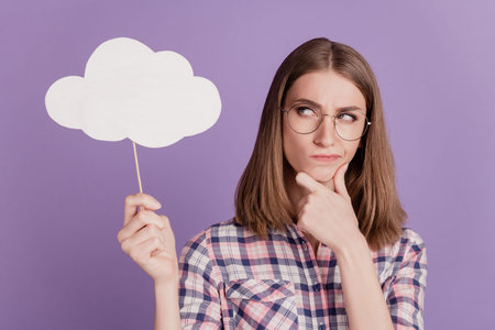 Portrait of attractive lovely lady hand touch chin think deep unsure hold clouds bubble isolated on violet color backgroundの写真素材