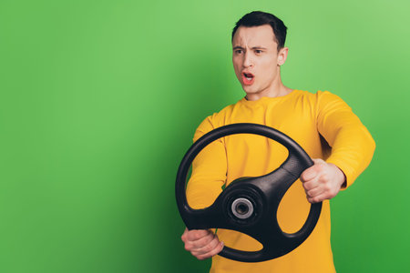 Portrait of crazy mad driver guy hold steering wheel shocked face on green background