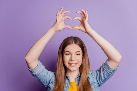Photo of charming affectionate girl making heart sign raise hands on violet background