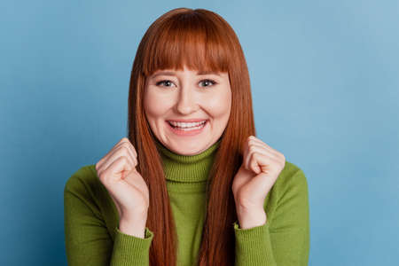 Portrait of funny dreamy girl cheerful toothy smile hold fists on blue backgroundの写真素材