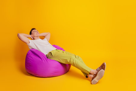Portrait of relaxed sleepy inspired guy sit beanbag hands head dream look up blank space on yellow backgroundの写真素材