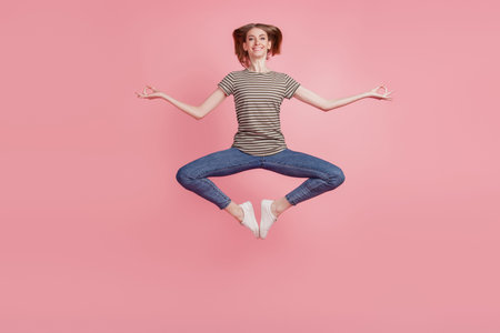 Full size portrait of young woman happy positive smile meditate yoga zen om jump up isolated over pink color backgroundの写真素材