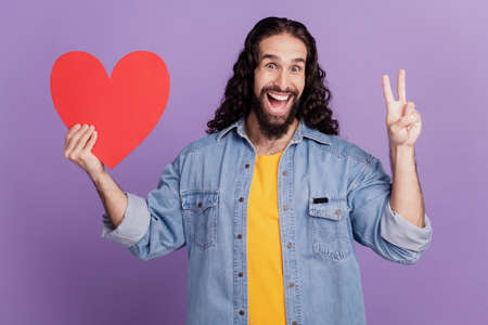 Closeup of friendly guy show v-sign hold red paper heartの写真素材