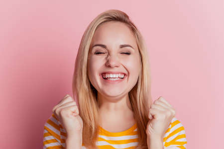 Portrait of excited astonished lady raise fists toothy smile on pink backgroundの写真素材