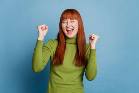 Portrait of shouting in winning with raised fists young girl isolated on blue backgroundの写真素材