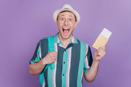 Portrait of cheerful positive pleased guy hold flight tickets scream open mouth on violet backgroundの写真素材