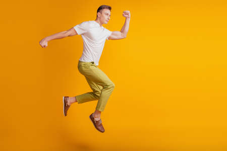 Portrait of funky positive guy jump fly run fast empty space on yellow backgroundの写真素材