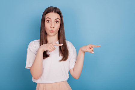 Portrait of excited girlish teen lady forefingers direct empty space on blue background