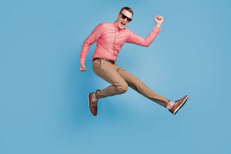 Portrait of astonished excited cool guy jump run winner concept on blue backgroundの写真素材