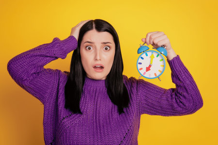 Photo of young girl shocked surpised deadlinehand touch head hold clock alarm timer isolated over...