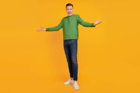 Portrait of friendly charming successful guy open hands posing look camera on yellow backgroundの写真素材