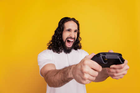 Portrait of crazy excited guy hold gamepad play videogame on yellow backgroundの写真素材