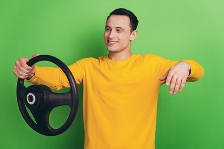 Portrait of confident guy hold steering wheel pretend drive car on green background
