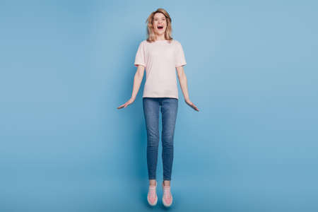 Portrait of funky crazy sportive nice lady jump crazy fun open mouth on blue backgroundの写真素材