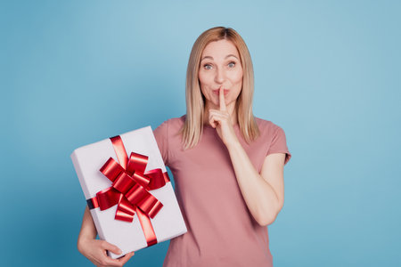Photo of young attractive woman cover lips finger shh surpise present box celebration isolated blue color backgroundの写真素材