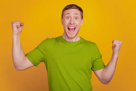 Excited and happy young adult man fists up smiling wide standing winner isolated on yellow background in casual t-shirtの写真素材