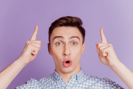 Portrait of excited shocked guy direct fingers up empty space open mouth on violet background