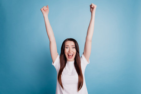Photo of amazed shouting with raised fists young girl isolated on blue background