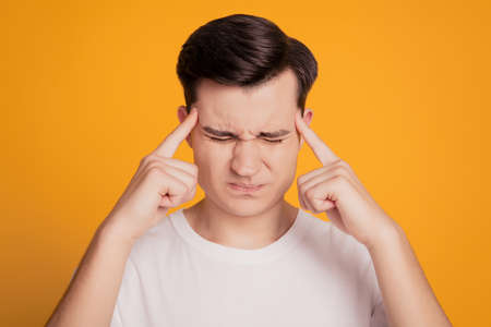 Portrait of troubled exhausted guy suffer headache fingers temples on yellow backgroundの写真素材
