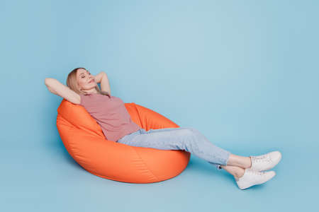 Photo portrait full body view of sitting in orange bean bag chair rest relax sleep nap time isolated on blue colored backgroundの写真素材