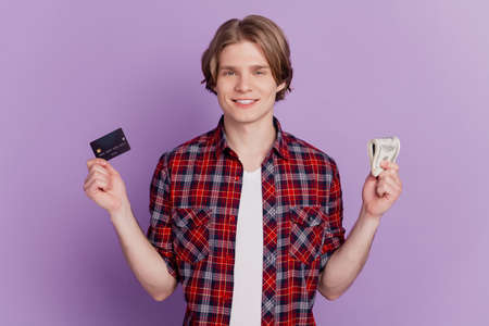 Portrait of cheerful guy hold debit card cash pile currency banknotes toothy smile on purple backgroundの写真素材